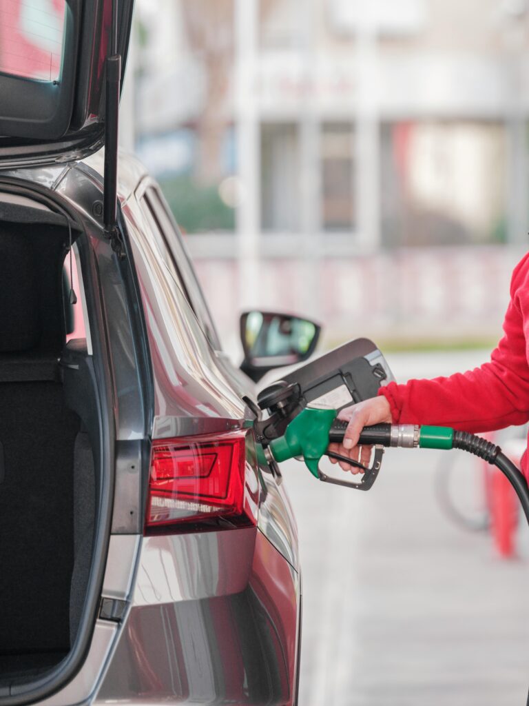 Close-up of a person refueling a vehicle at a gas station with a green fuel pump.